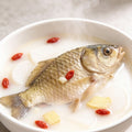 Whole crucian carp simmering in a milky-white fish soup with goji berries and ginger