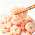 Pile of peeled shrimp meat on a white plate with chopsticks lifting one piece