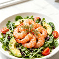 Cooked sweet shrimp arranged over a salad of rocket, avocado and cherry tomato