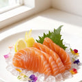Salmon sashimi slices fanned on crushed ice with a shiso leaf, lemon wedge and edible flowers