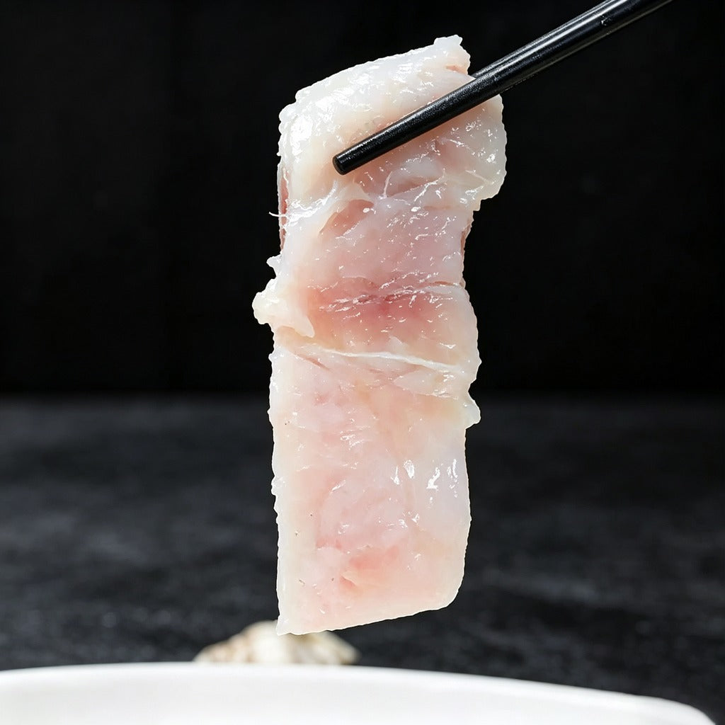 A thick slice of raw white fish held up with chopsticks, showing pink-tinged flesh